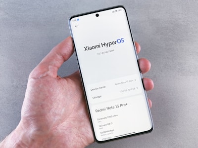 Hand holding a smartphone displaying xiaomi hyperos information.